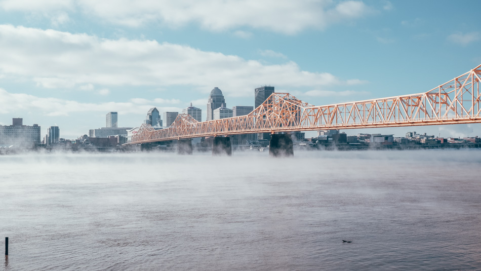 Bridge stretching over the Ohio River towards the Louisville skyline as steam rises from the river on a winter day in Louisville, Kentucky